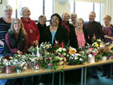 A group standing behind a long table of flower arrangements they have made